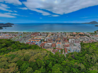 Vista aérea de Ubatuba, mostrando a orla da cidade com praias paradisíacas, mar azul e Mata Atlântica preservada, destacando o crescimento do turismo internacional na região.
